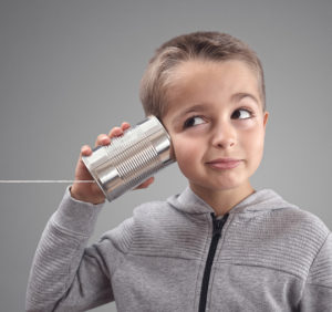 young boy holding tin can with string attached to his ear